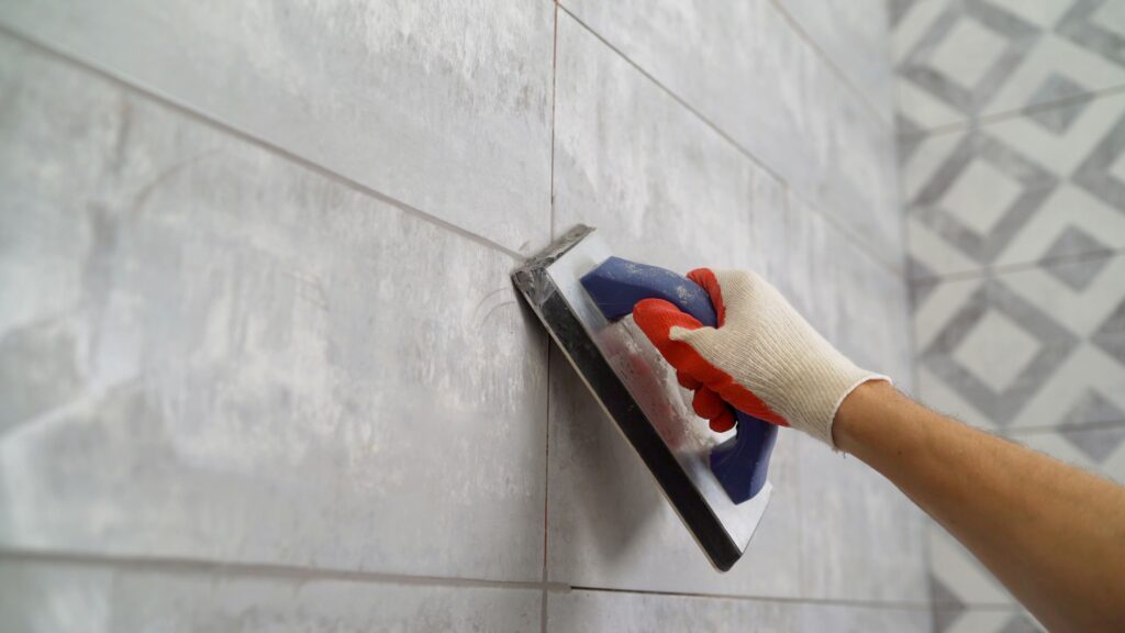 man placing grout in between tiles in bathroom